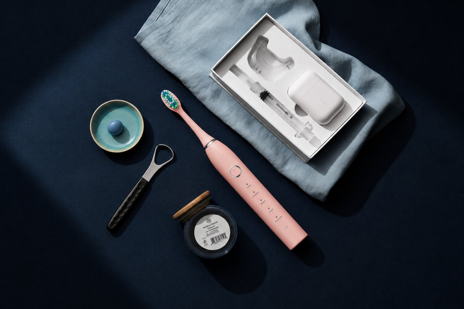 Snosha oral care bundle flat lay: N2 pink toothbrush, teeth whitening kit and tongue scraper on dark background