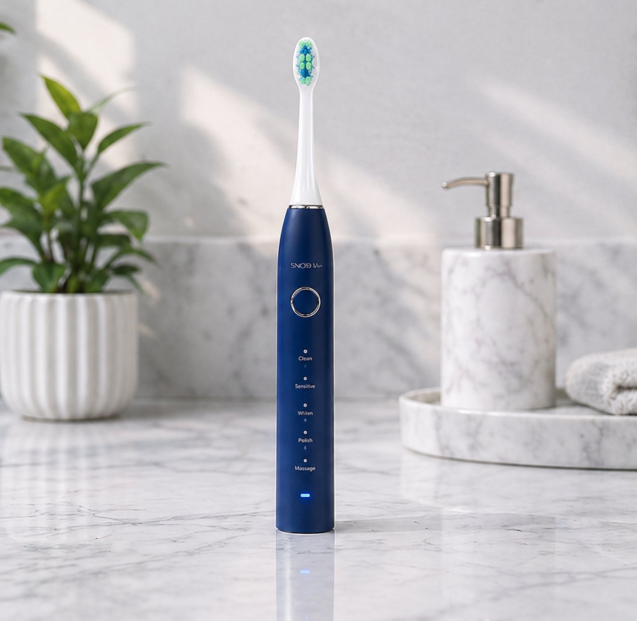 Snosha N2 blue electric toothbrush on marble bathroom counter with plant and soap dispenser